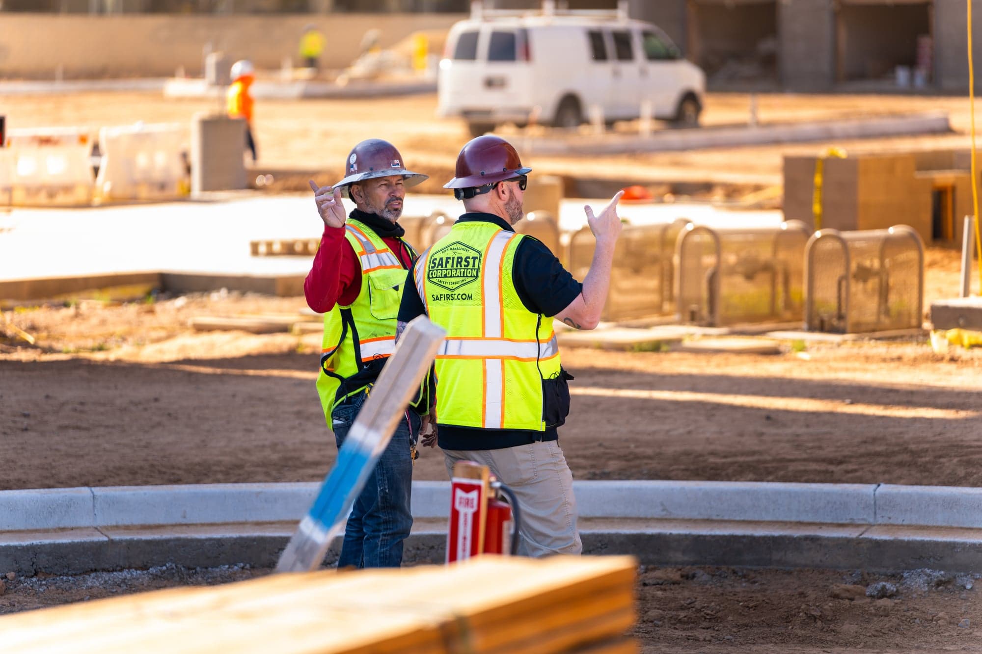 Safety consultant gesturing as he coaches a worker on a graded pad, a fire extinguisher stand in the foreground